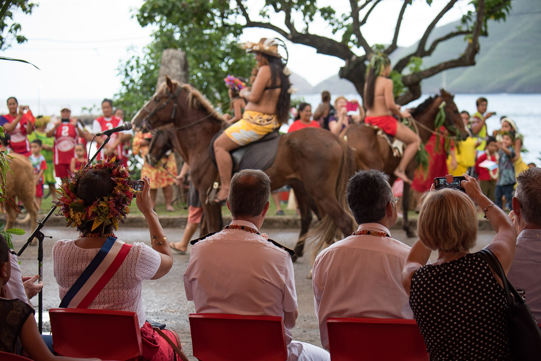 A crowd of people watch as men and women on horses pass by during a ceremony.
