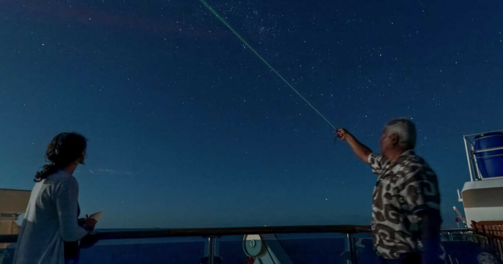 Two people on a ship's deck at nigh looking at stars.